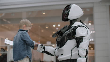 the boy stretches out his hand to the robot for a handshake