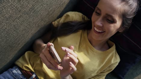 Top-view-of-caucasian-woman-lying-on-sofa-and-browsing-phone