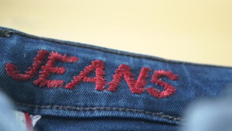 close-up of jeans with red embroidered "jeans" text