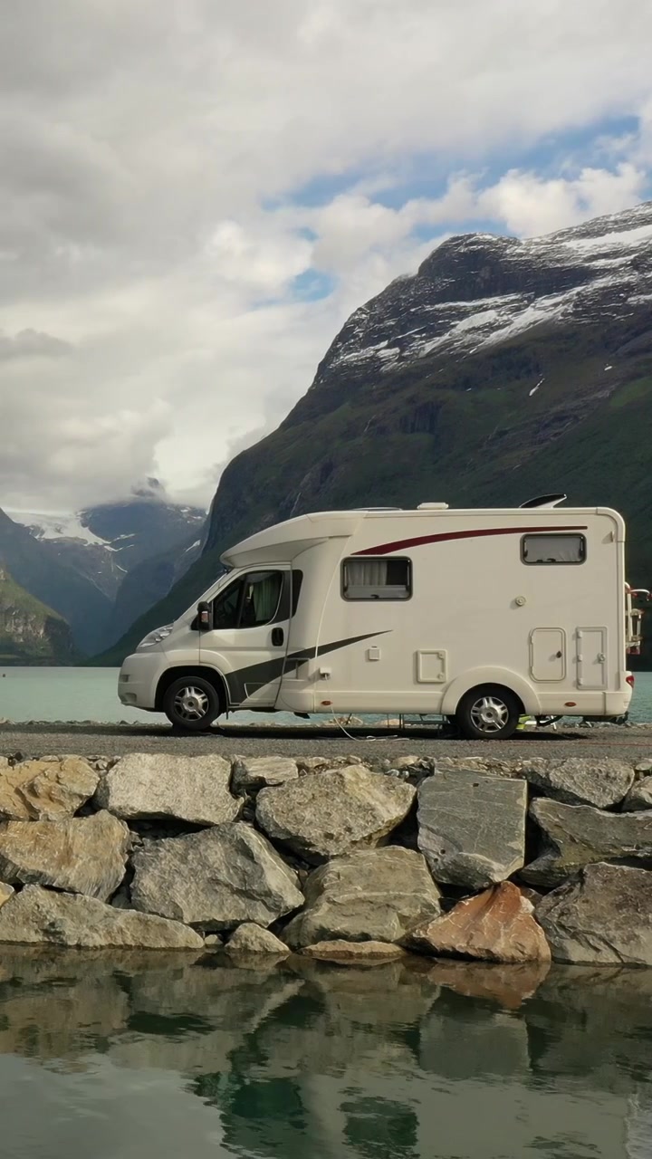 Motorhome parked by mountain lake in dramatic alpine landscape, vertical travel scene.