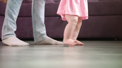 little baby feet walking on floor with parent support. kid feet steps at home