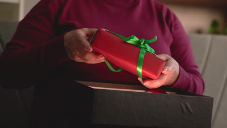 Nahaufnahme-Der-Hände-Einer-Frau,-Die-Ein-Weihnachtsgeschenk-Aus-Einer-Kiste-Herausnimmt,-Die-Auf-Dem-Sofa-Sitzt