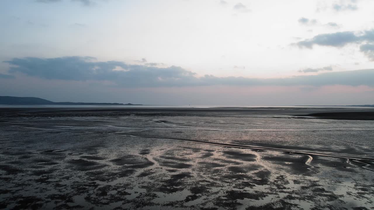 aéreo: dolly lento hacia el horizonte del atardecer sobre arena texturizada, llanelli, dron 4k