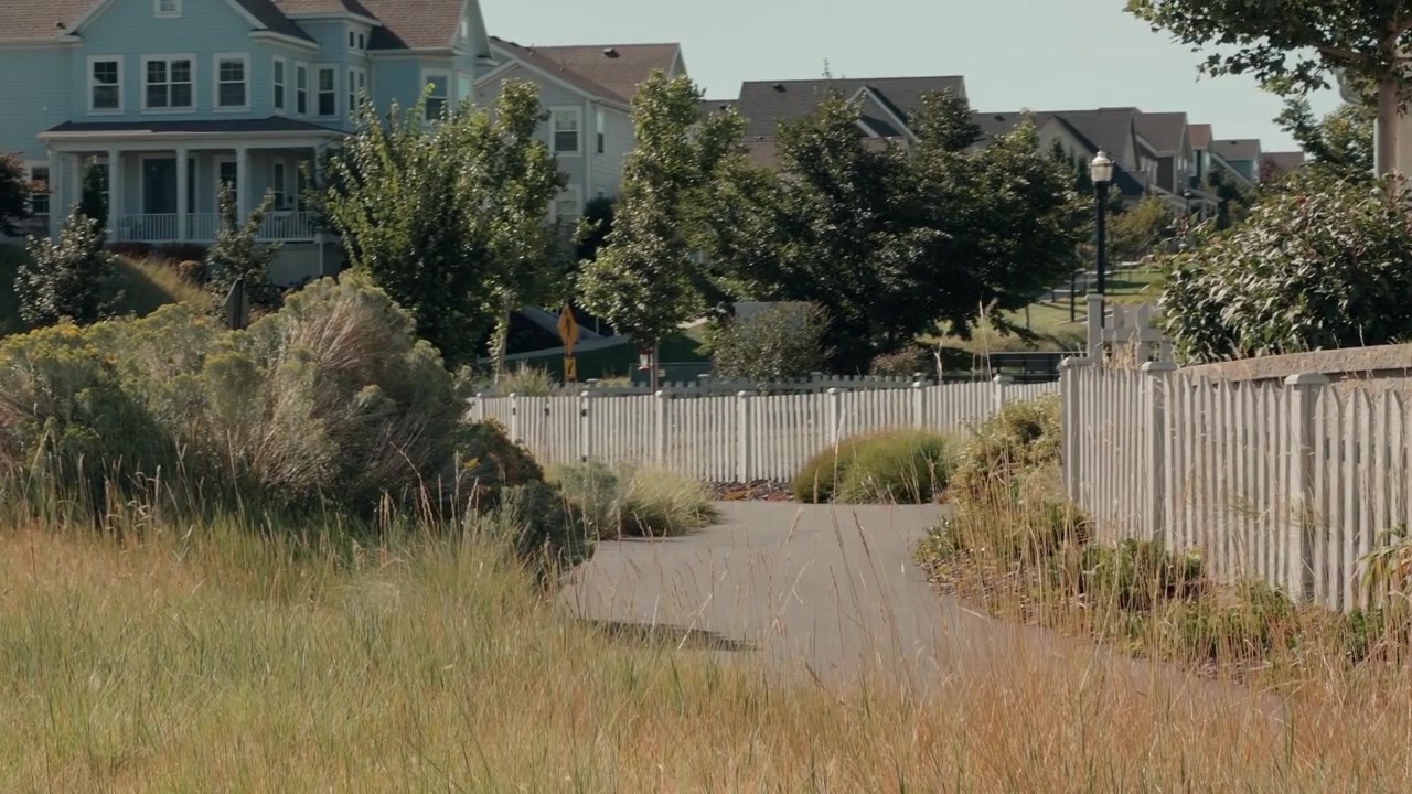 Still view of a quiet park trail surrounded by houses and greenery.