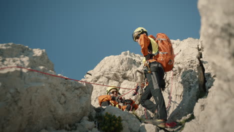 Lower-perspective-of-two-hikers-tieing-rope-for-a-secure-descent-from-the-mountain,-clear-blue-sky