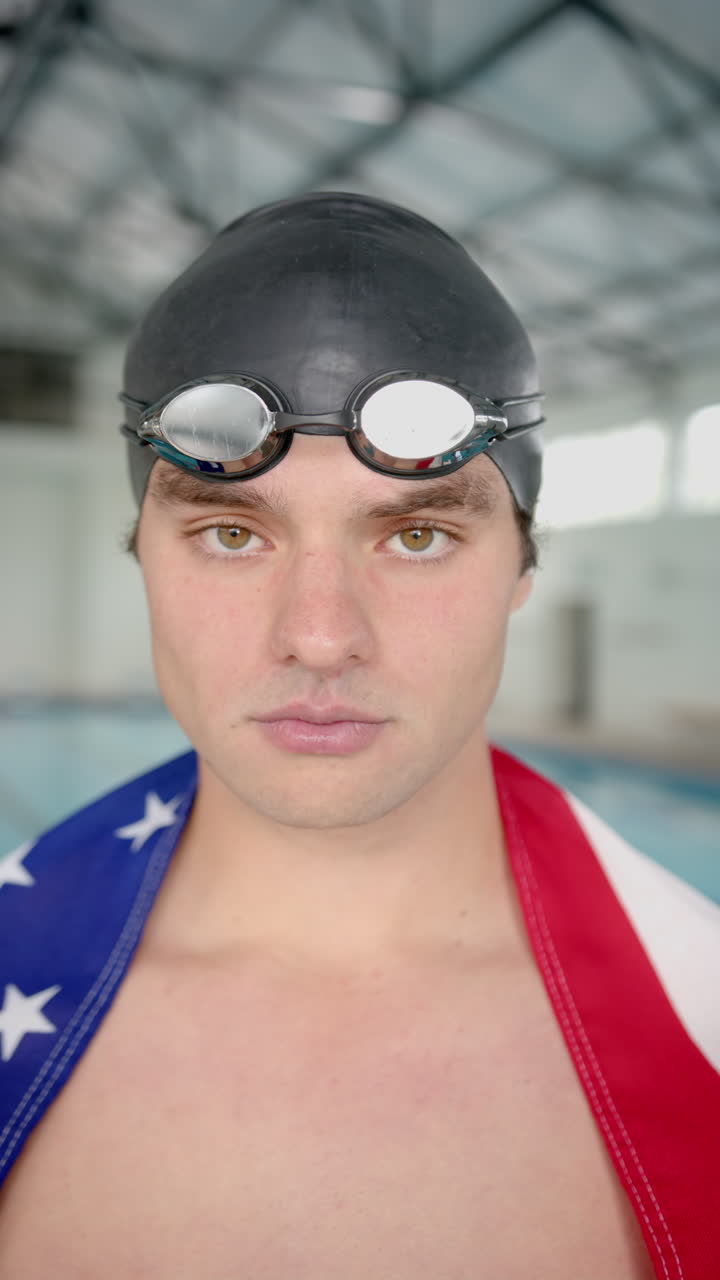 Vertical video: Swimmer wearing goggles and swim cap, wrapped in American flag by poolside