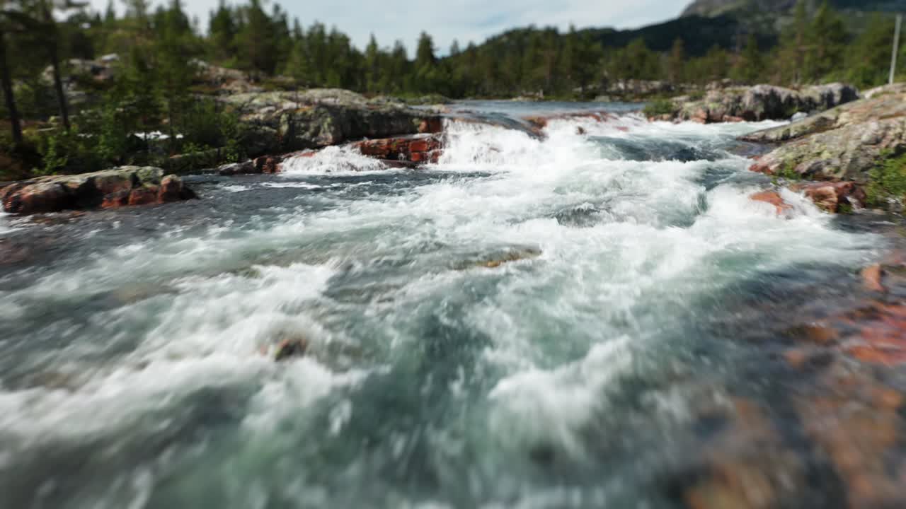A flight against a current over powerful waters of a mountain river running over a layered stone bed in Norway