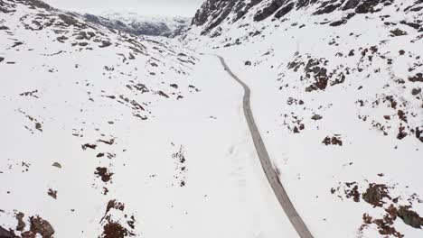 dramatic landscape at mountain road crossing during harsh winter - unknown car passing in the distant