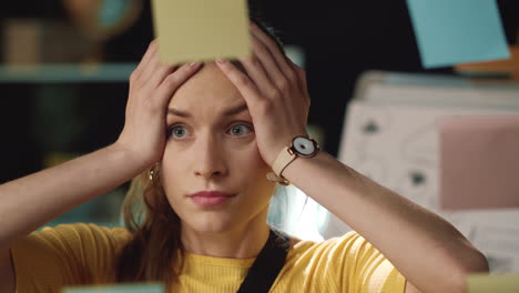 exhausted hipster woman grabbing head near transparent wall in modern workplace.