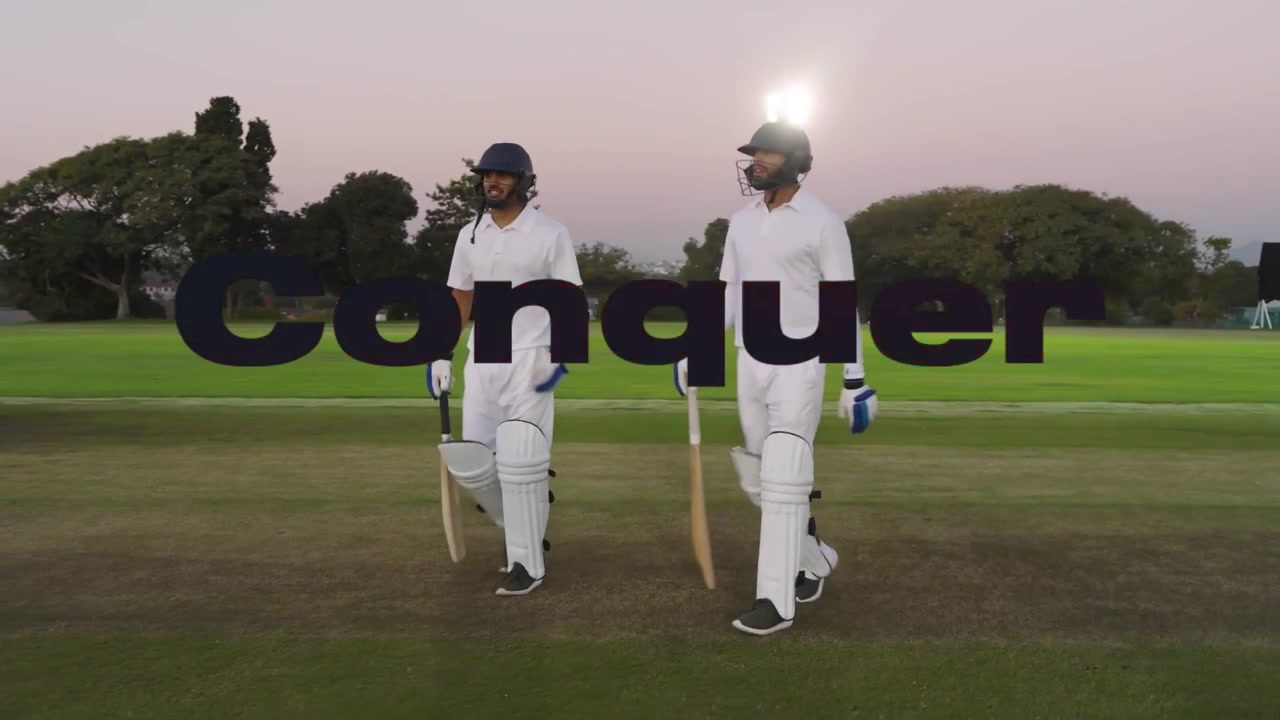 Due battitori di cricket che entrano in campo, toccandosi le mazze come partner, camminando sotto una sovrapposizione rossa Conquer.