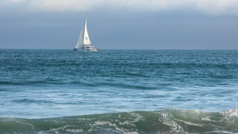 Seitenansicht-Eines-Katamaransegelboots,-Das-In-Vollen-Segeln-Auf-Einem-Dunkelblauen-Meer-Mit-Reflexionen-Im-Gegenlicht-Segelt