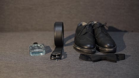 man groom takes belt from sofa with perfume, black bow tie, shoes. businessman in wedding morning