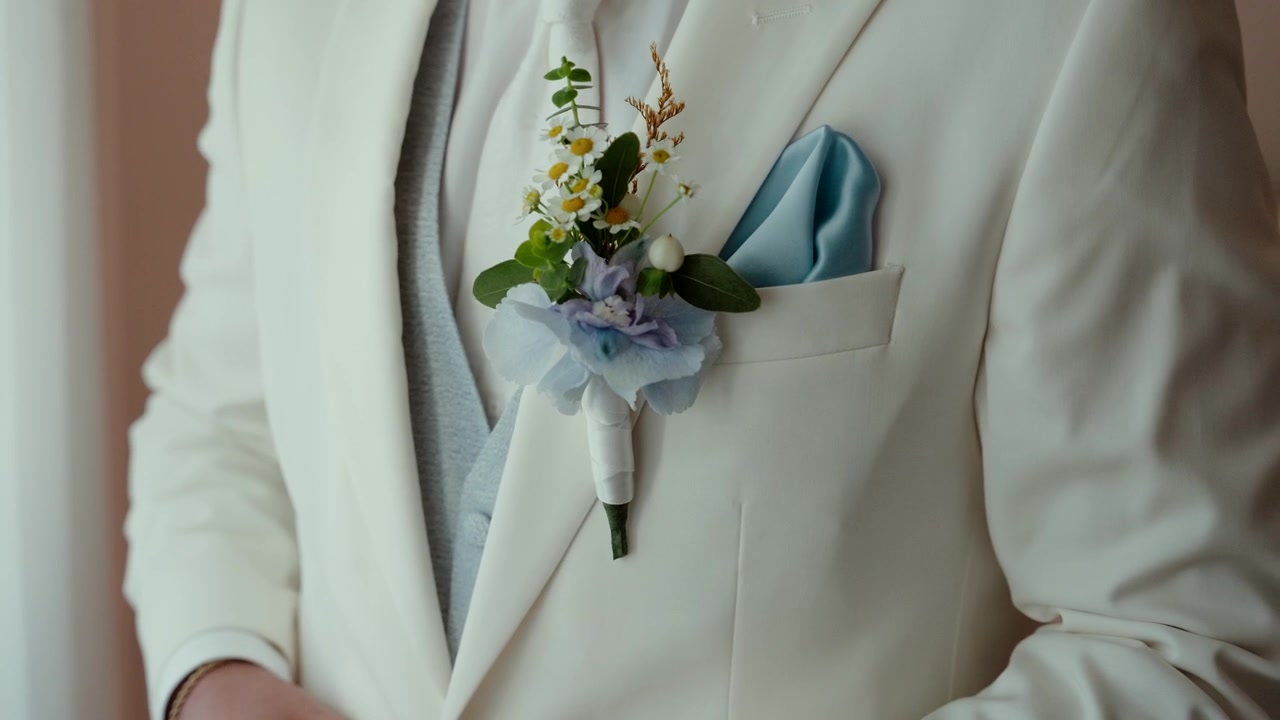 Boutonnière de margarida e hortênsia preso em um terno de casamento creme com lenço de bolso azul