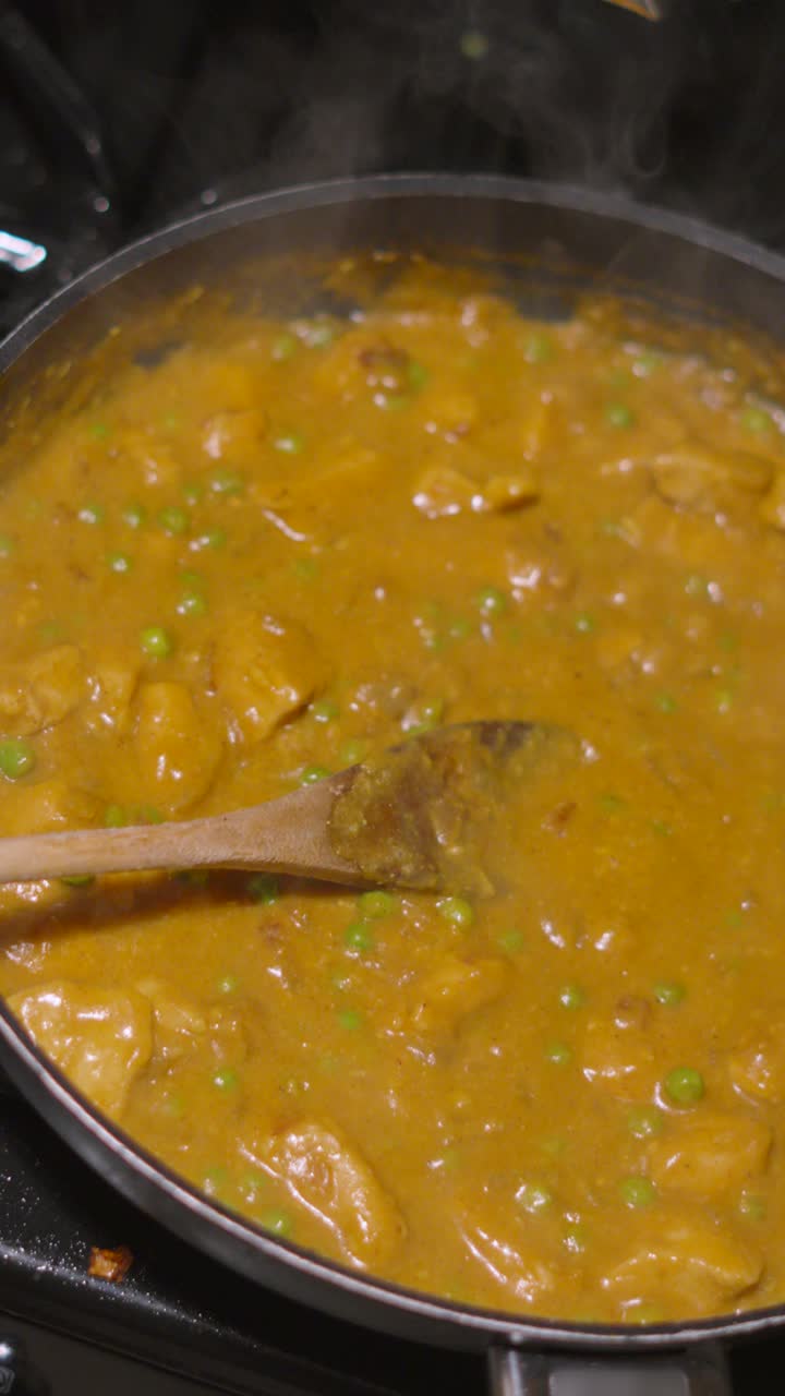 Video verticale. Filmato al rallentatore dall'alto di un cucchiaio di legno appoggiato su un curry korma di pollo dorato. Il vapore sale mentre la salsa a base di cocco sobbolle