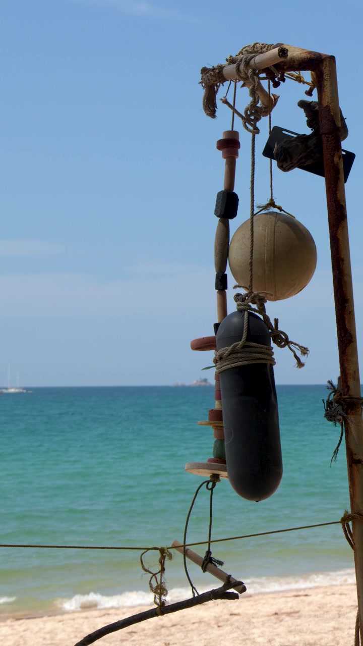 Inquadratura media statica di boe consumate dalle intemperie appese a un palo di metallo arrugginito su una spiaggia soleggiata