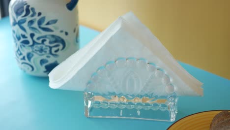 glass napkin holder with white napkin on a blue table