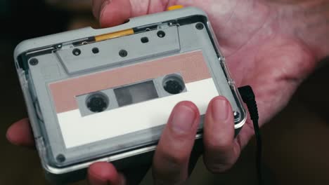 close up of a man's hand inserting a cassette tape into a cassette player.