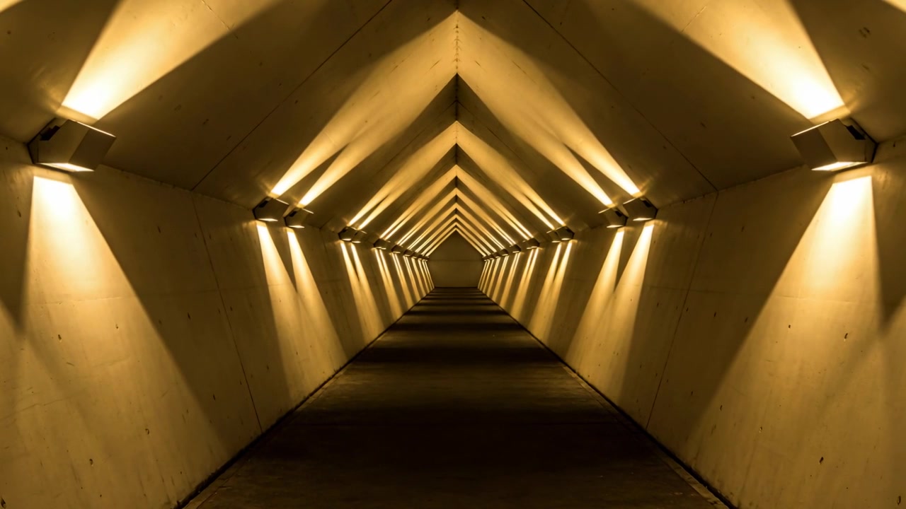 Carrellata della telecamera che rivela un tunnel di cemento in un sottopassaggio, mostrando volte triangolari e applique.