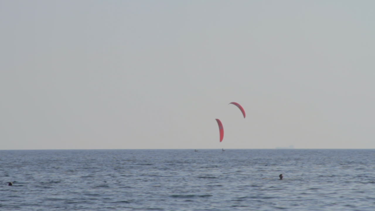 два кайт-серфера проплывают мимо катамарана, недалеко от пляжа