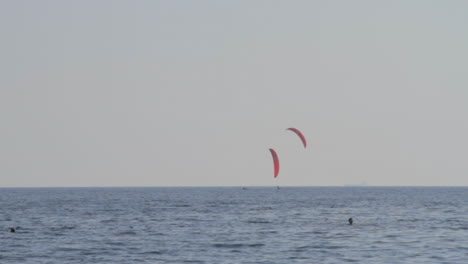 two kite surfers sail by a catamaran, near the beach