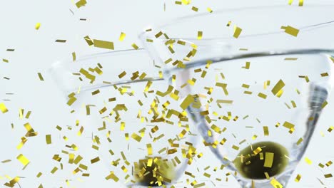 Golden-confetti-falling-over-olives-in-two-in-cocktail-glasses-against-grey-background