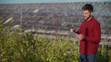 farmer writing notes in greenhouse close-up