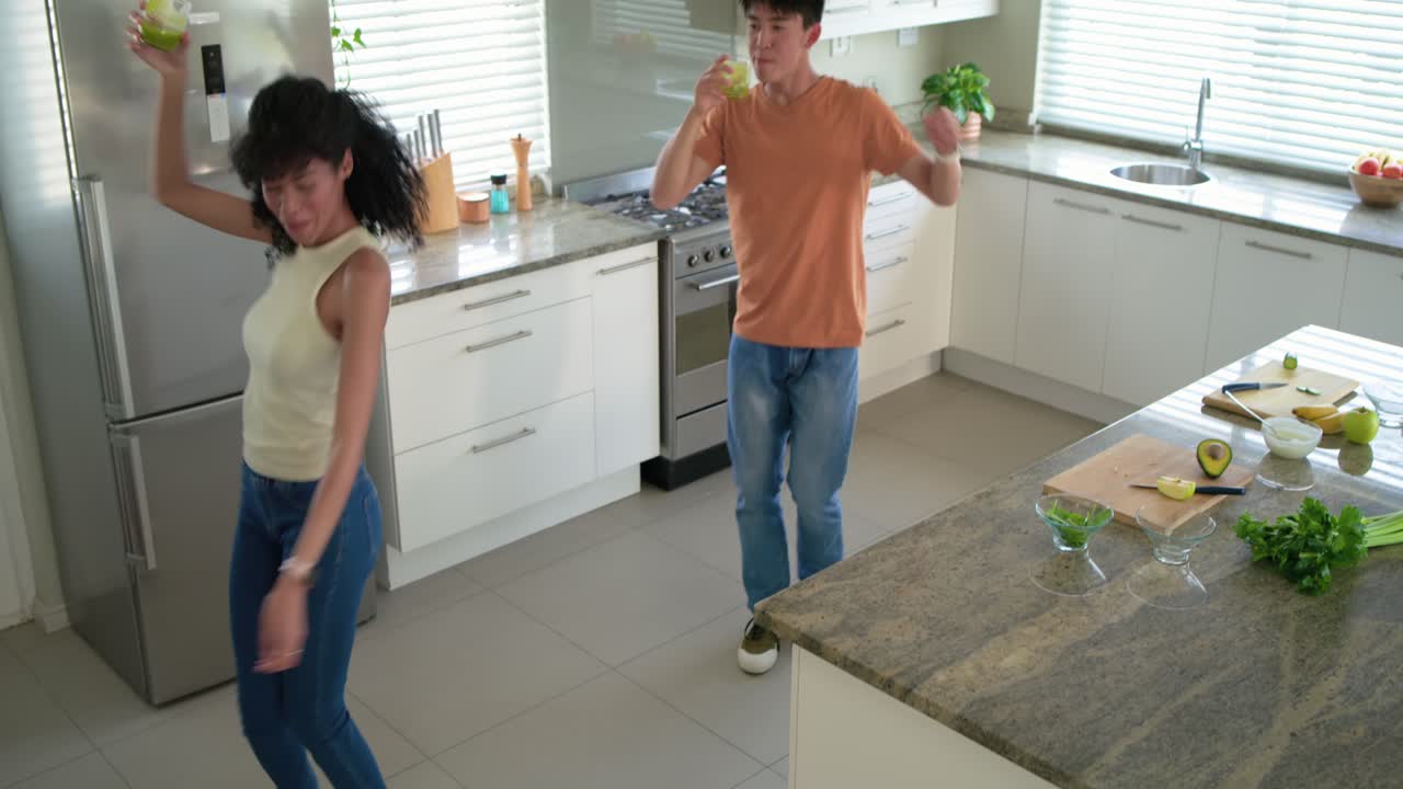 Couple dancing with beat starting in bright kitchen, toasting with green-drink glasses and sipping
