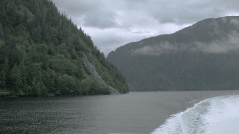 an alaskan fjord with a mountainside in the foreground, filmed from the back of a boat creating smooth motion with a settling wake