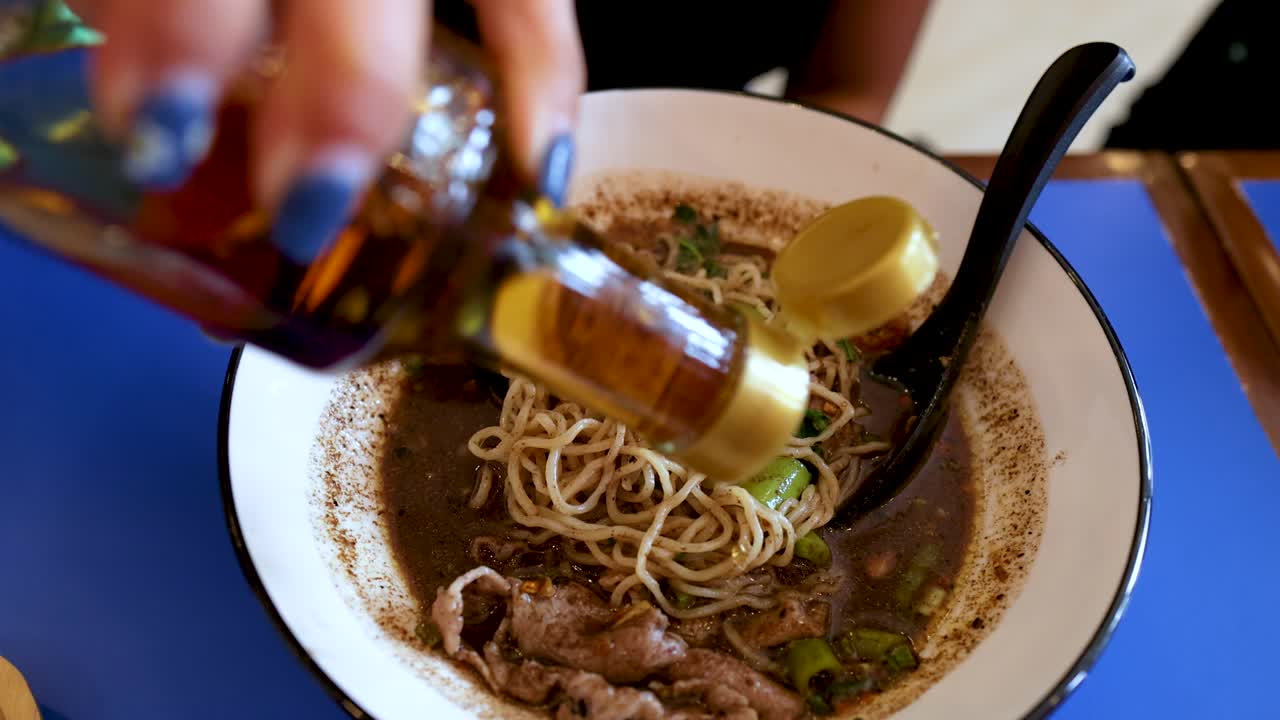 Un primo piano mostra condimento liquido versato da una bottiglia in saporiti noodles tailandesi in barca