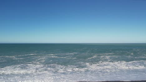 slow and low aerial approach towards small incoming waves rolling onto stony beach - birdlings flat, beach