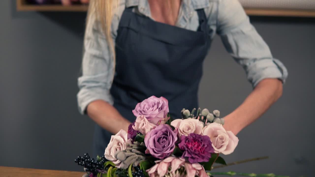 Portrait of a young flower shot assistant tying a bunch of flowers lying on her table with the ribbon. Slow Motion shot