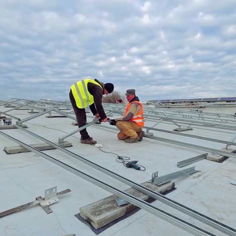 workers building metal basis under blue cloudy sky. two engineers in uniform constructing metal base for solar power plant on a roof.