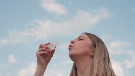 close up side view woman blowing bubbles under clear blue sky over open farmland capturing carefree outdoor moment with shimmering soap spheres drifting against soft clouds