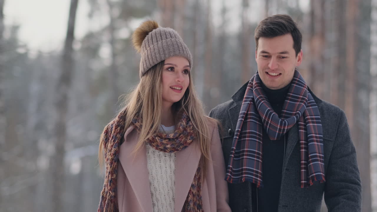 Young married couple in love walking in the winter forest. A man and a woman look at each other laughing and smiling in slow motion. Valentine's Day love story.