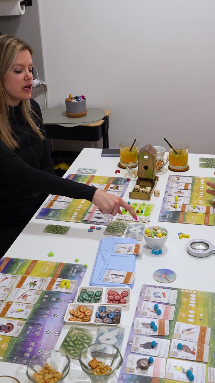 Scatto verticale di una famiglia che gioca a una serata giochi con il gioco da tavolo Wingspan in ambiente domestico.