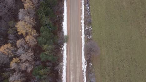 aerial shot of a dirt road lined with snow, forest and farm land