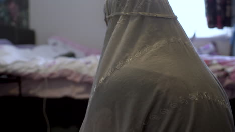 joven mujer musulmana con hiyab blanco agachándose para orar en el dormitorio