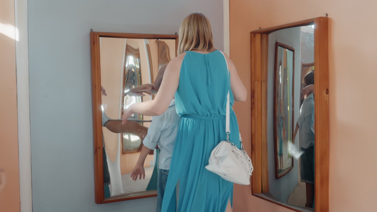 Ragazzo indaga un'immagine distorta nello specchio. Bambino in abito blu osserva il suo riflesso in uno specchio divertente e bizzarro. Giovane ragazzo interagisce con lo specchio deformato mentre sua madre lo osserva gentilmente nelle vicinanze.