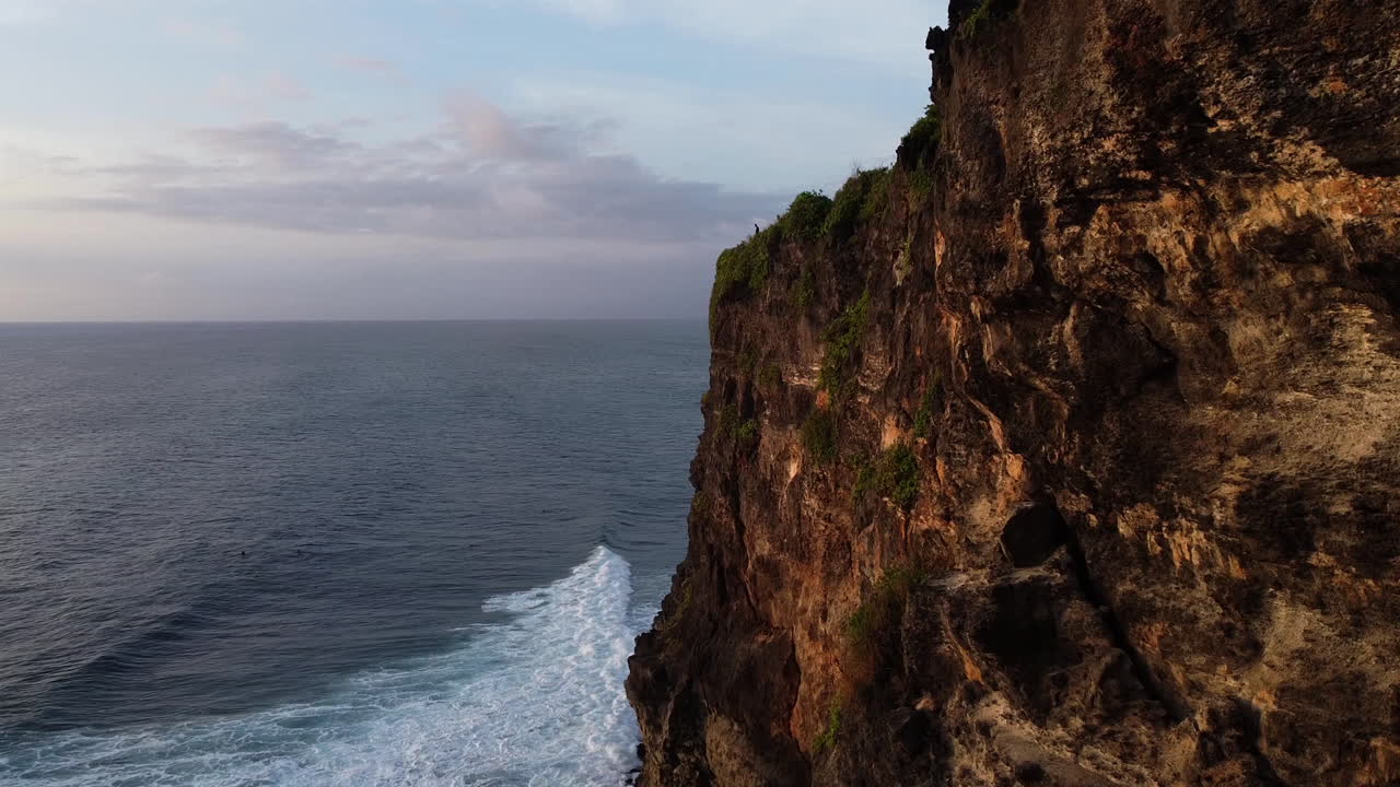 Drone shot flying down the past cliff towards the ocean in Uluwatu, Bali