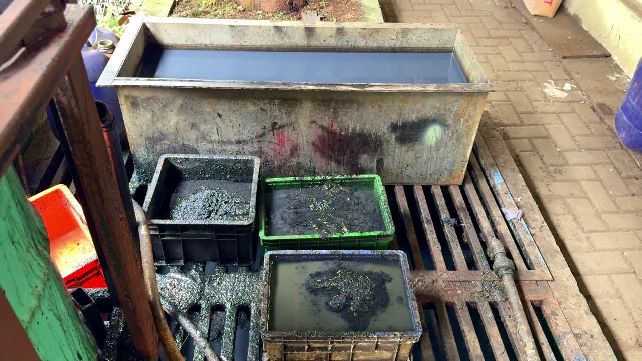 Footage of industrial waste sludge stored in plastic and metal containers, showing contaminated water and residue from factory production