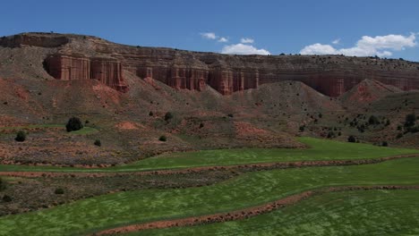 Vista-Aérea-De-Drones-De-Campos-De-Grano-Verde-Ondeados-Por-El-Viento-En-Un-Cañón-Rojo-Postre-En-Teruel,-España