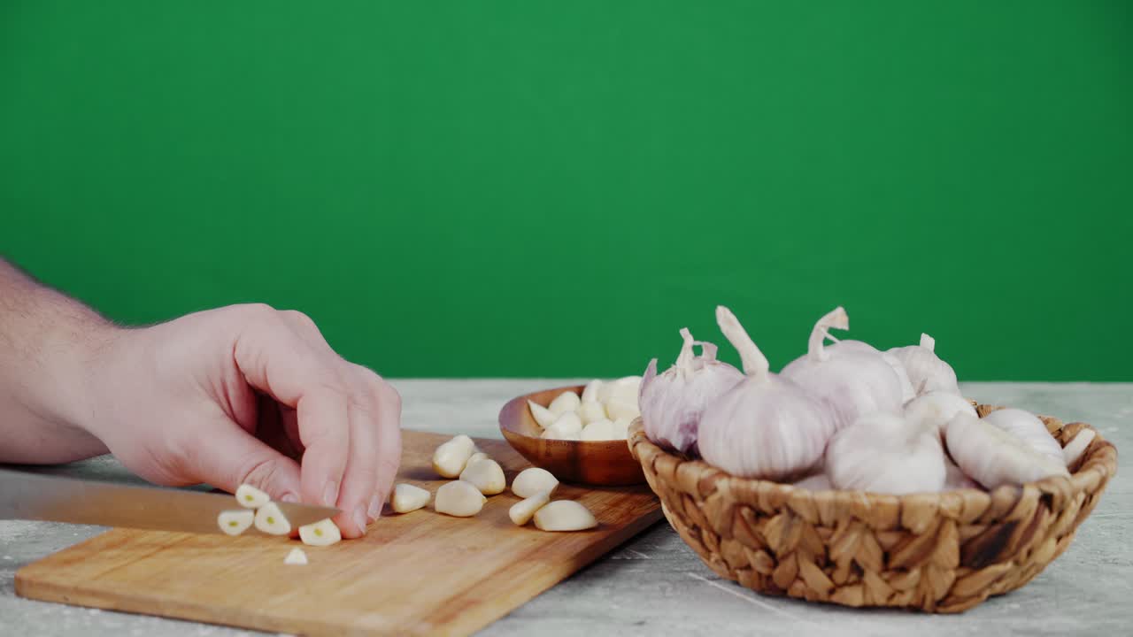 Male hand with a knife cut the garlic into pieces.