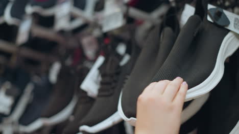 vista de la mano de la dama en vestido rosa en la tienda de zapatos examina de cerca la suela de zapatillas negras con sus dos manos, mientras que los estantes llenos de varios zapatos están ligeramente borrosos en el fondo, la tienda está bien iluminada