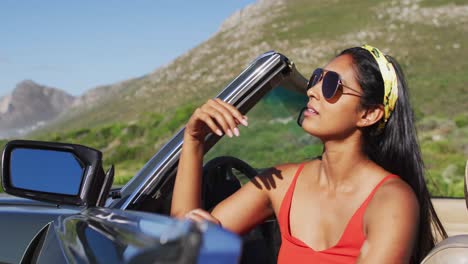 mujer afroamericana con gafas de sol sentada en el coche descapotable en la carretera