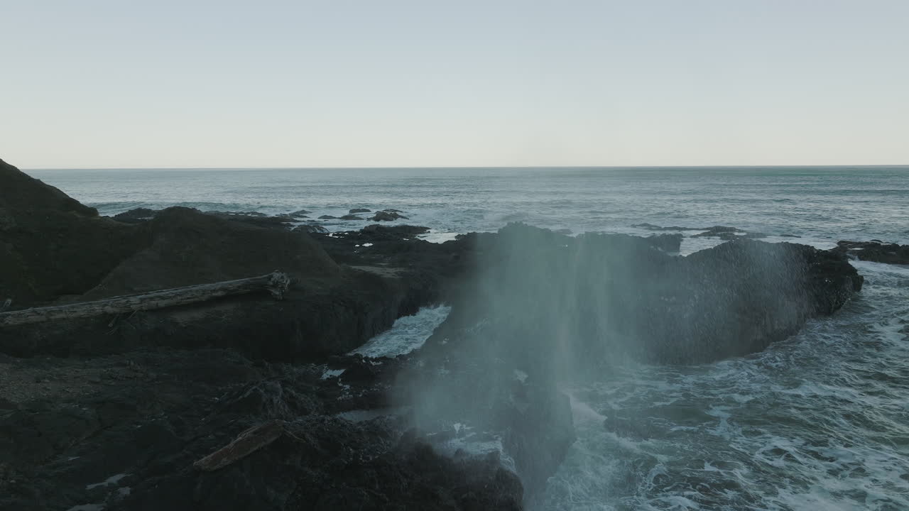 las olas chocan en la costa de oregón y el agujero de soplo lanza el agua hacia arriba en una hermosa niebla al amanecer.