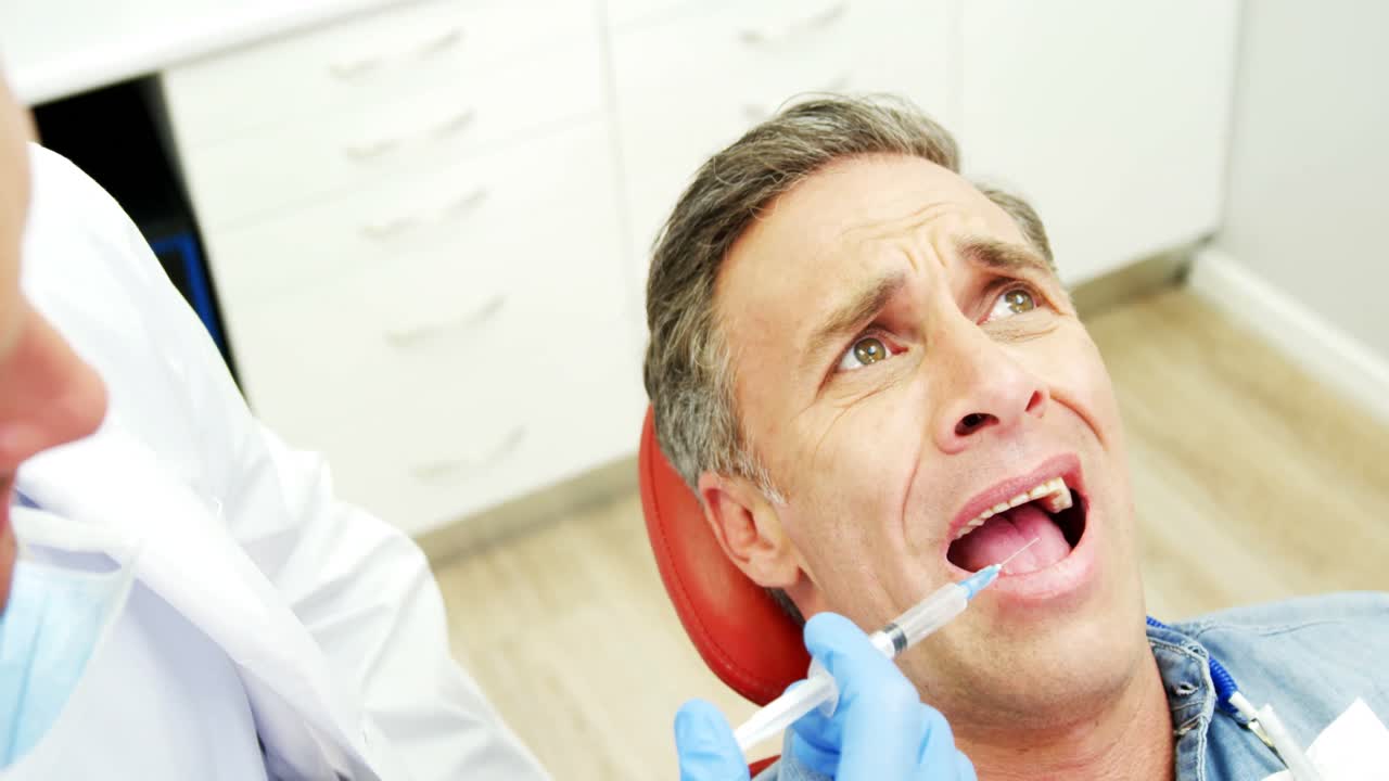 겁에 질린 남자가 치과의사로부터 주사를 맞고 있습니다.