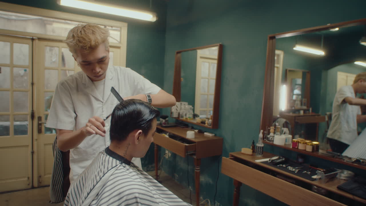 Barbiere asiatico che taglia i capelli a un cliente in un salone da barbiere