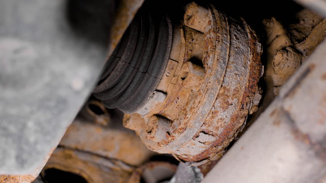 Close up of rusty bolts and driveline parts under a used car. Rotating movement shot in 4k.