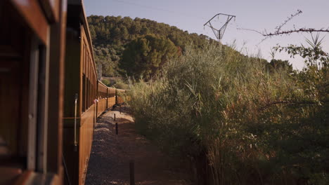 Old-vintage-wooden-Soller-Train-in-Mallorca-driving-through-wilderness-on-a-sunny-day