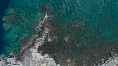 Aéreo:-Drone-Mirando-Hacia-Los-Acantilados-Rodeados-De-Olas-Y-Agua-De-Mar-Turquesa